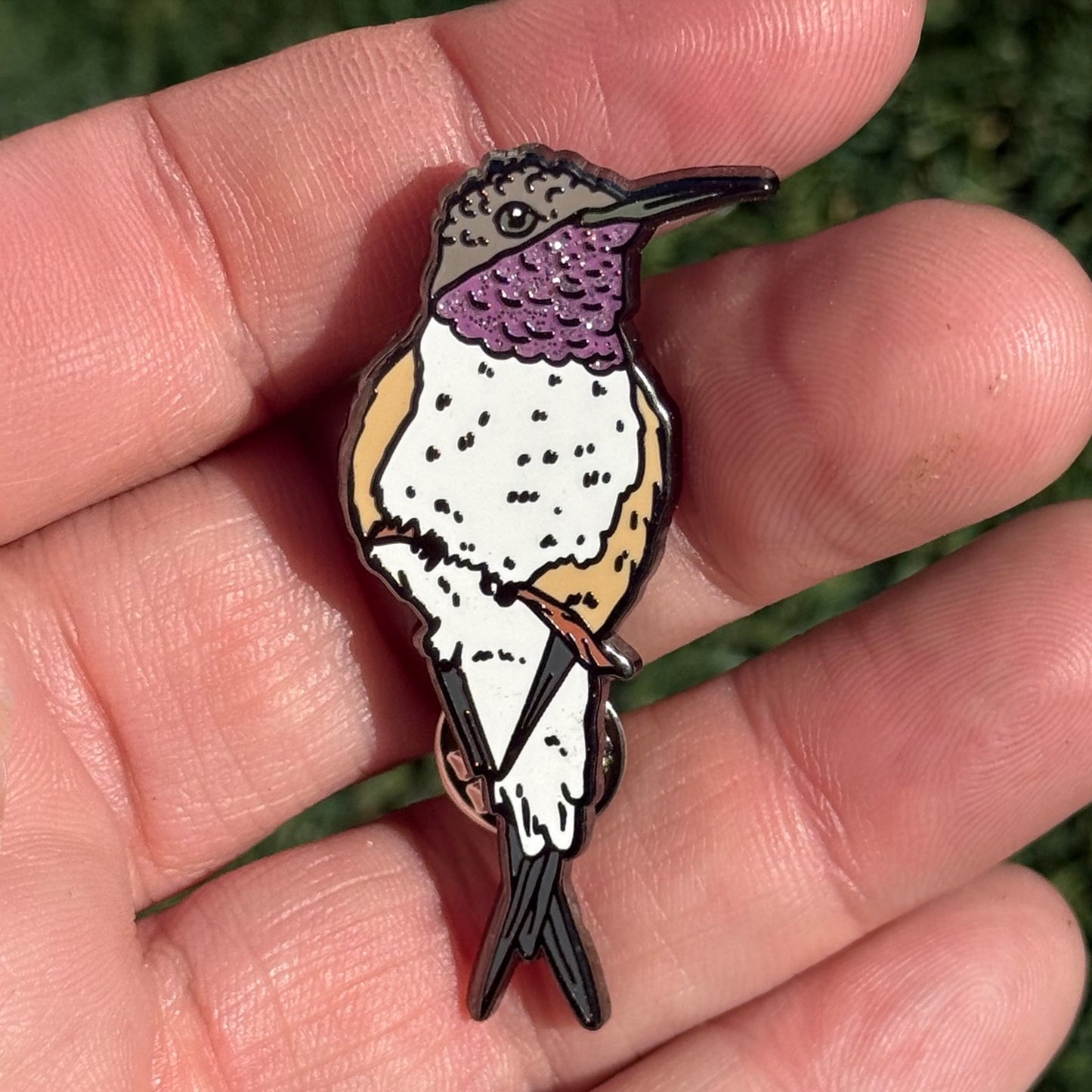 Chilean Woodstar glitter enamel pin shown in hand